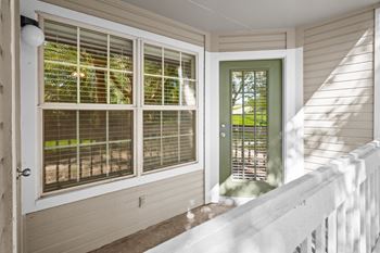 A private balcony with white railing, large windows, and a green door.